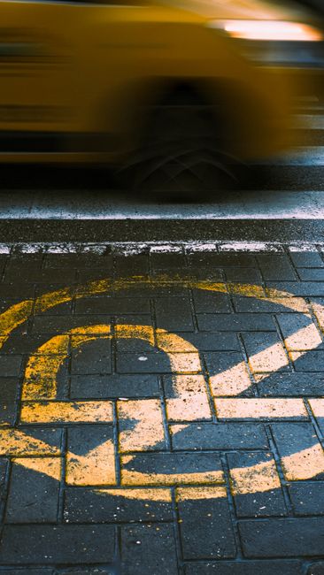 Close-up view of a concrete sidewalk with a white painted circular symbol featuring a bicycle crossed out, indicating no bicycle riding permitted. Beneath the symbol, the text reads 'NO BICYCLE RIDING ON SIDEWALK'. The sidewalk consists of large rectangular slabs with visible expansion joints, and the surface shows slight texture and weathering. This image may be relevant to house removals or moving logistics when considering pedestrian and cyclist regulations in residential or urban areas, as seen in the context of parking and pavement rules for Mill Hill moves, as detailed on the page from Man with Van Mill Hill.
